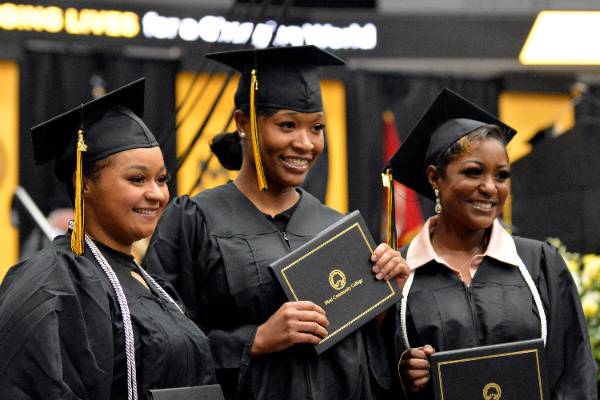Three MCC women graduates in cap and gowns posing with their diplomas at the commencement ceremony.