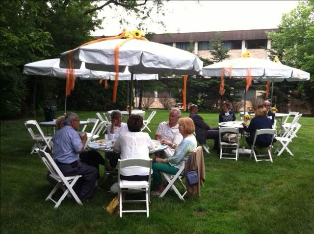 Guests at tables under umbrellas on the lawn.