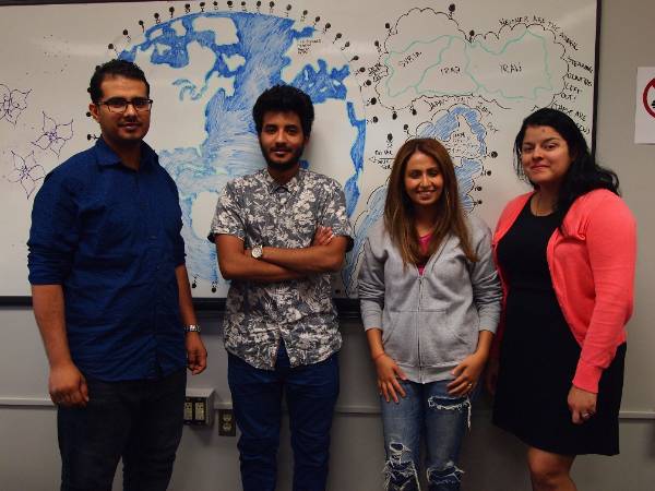 4 students standing in front of hand drawn world map