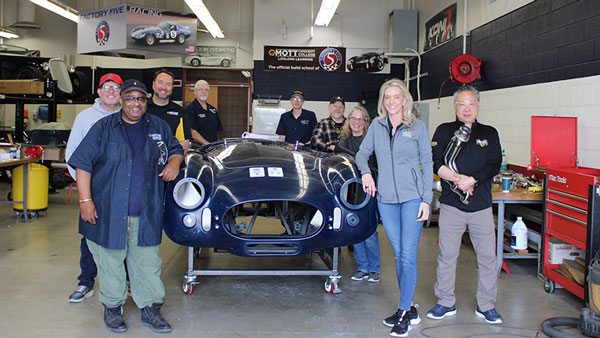 The President, her Executive Cabinet Members and instructors standing around the project car chassis in the Regional Technology Center on the main campus.