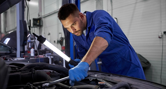 Male mechanic working under the hood of a car holding a light stick