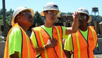 Group of three young men in wearing hard hats and safety vests conversing outdoors at a job site