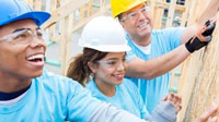 Young man, young woman and older man in light blue t-shirts and hard hats working on a building construction site